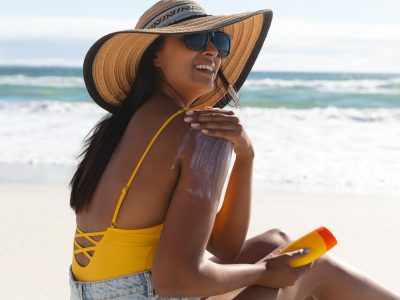 A young woman sits on the beach and applies sunscreen to her shoulders to prevent sunburn, following smart skin care tips