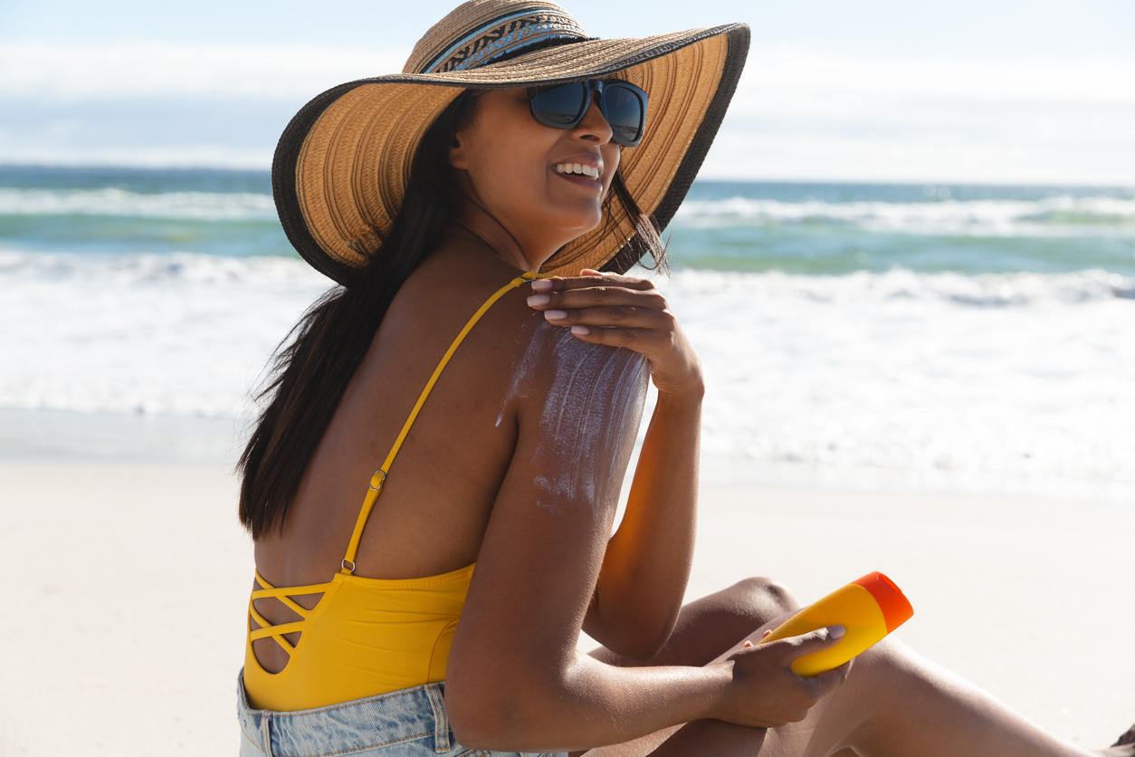 A young woman sits on the beach and applies sunscreen to her shoulders to prevent sunburn, following smart skin care tips